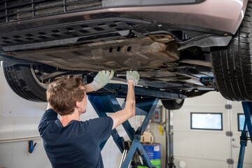 car mechanic standing under lifted car and fixing car in garage