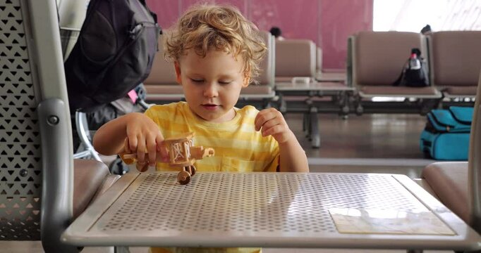 Full throttle! Toddler boy plays with wooden toy biplane at airport, passing time before boarding his flight. He spins small wooden propeller with his hand, watching it turn.