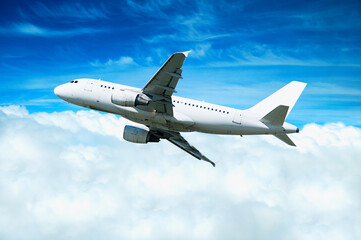 Airplane in the flight, travel background with modern white airplane flying in the blue sky high over the clouds. Flying airplane with blank white livery