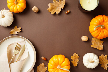 Autumn cozy table setting with pumpkins, candle, acorns, nuts and dry oak leaves on brown background. Flat lay, top view, copy space
