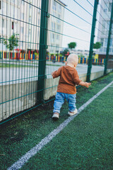 Cute toddler boy running on the soccer field. Active time of the child outside. A child runs on the street in the summer. A boy in jeans and a T-shirt. A stylish toddler