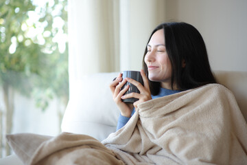 Fototapeta premium Asian woman in winter drinking coffee covered with blanket at home