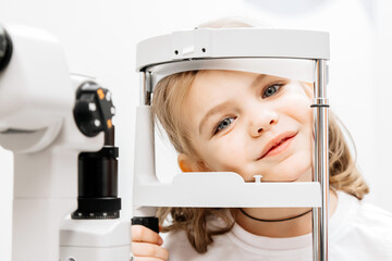 Close-up of a little girl with deep eyes undergoing vision diagnostics using a slit lamp in an...