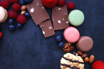 Macarons, chocolate, cookies, berries and various nuts on dark blue background. Top view.