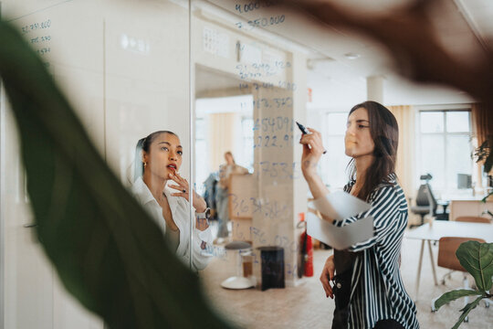 Female business colleagues preparing statistics while writing on glass board at office