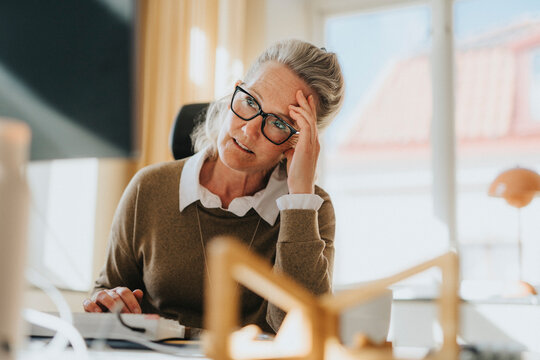 Exhausted businesswoman with head in hand while sitting at desk in office