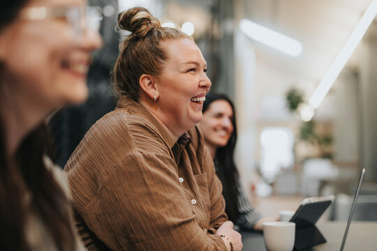 Happy businesswoman with hair bun sitting with female colleagues at office