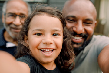 Close-up portrait of smiling boy taking selfie with father and grandfather
