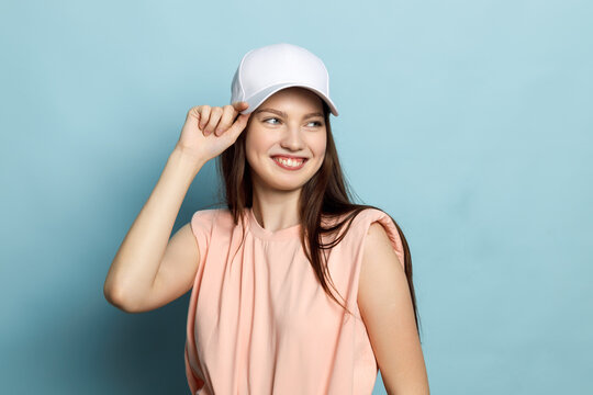 Young woman, teenager, model, posing in white cap and pink T-shirt on blue background. Sweet face, smiling, laughing.