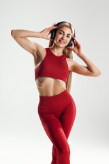 Young caucasian woman wearing headphones dancing active isolated on gray wall listening to music laughing cheerful