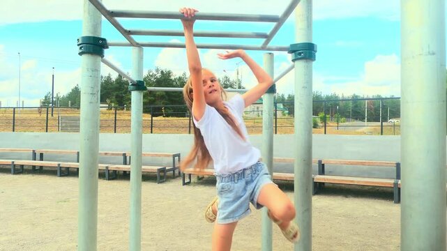 Little girl training on monkey bars hanging swinging from rung to rung as part of crossfit workout routine. Child girl doing toning exercises exercising arms.