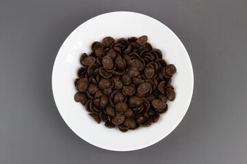 płatki czekoladowe w białym talerzu pośrodku na szarym tle. widok z góry.,  © Nina