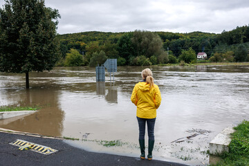 Flooded river. Worried woman looking at overflowing water during flood. Extreme weather and natural...
