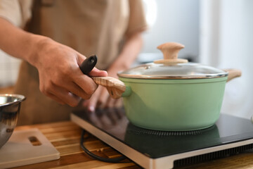Close up shot of man cooking in a green pot on a stove. People, food and domestic kitchen concept