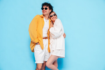 Happy beautiful romantic teenage couple. Smiling handsome caucasian man and young woman in summer clothes posing in studio, hugging sharing emotions, cheerful and happy. Isolated on blue