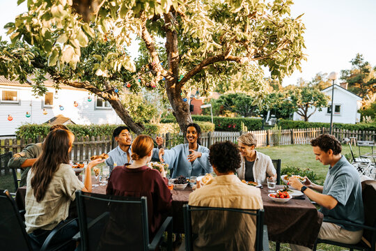 Male and female friends having dinner in back yard at social gathering - Powered by Adobe