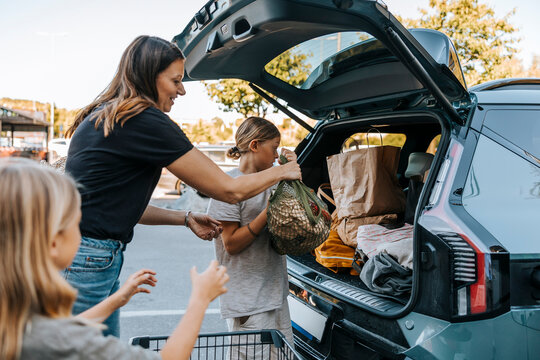 Boys helping mother loading grocery bags in car trunk at market