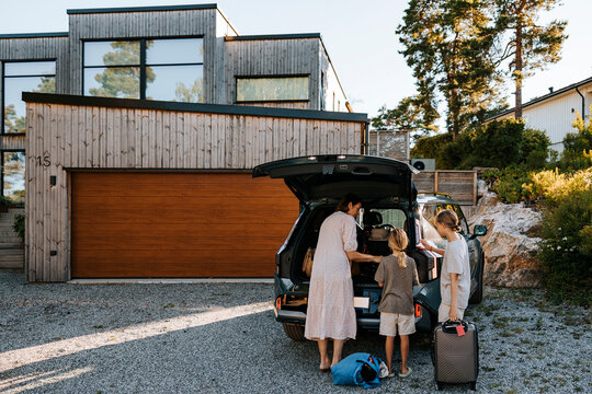 Mother and sons loading luggage in car trunk while standing in front of house