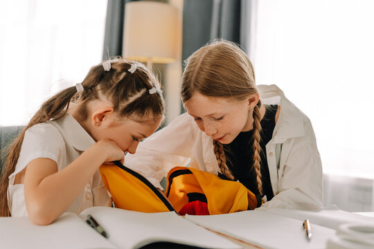 Two schoolgirls searching for something in backpack during studying at home