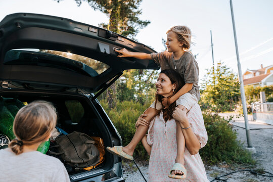 Son closing car trunk through push button while sitting on mother's shoulder
