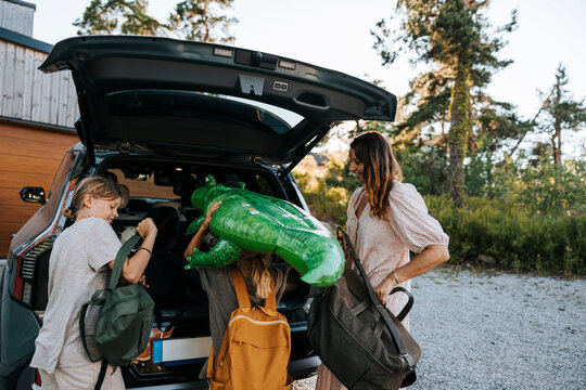 Boys loading luggage in car trunk with mother on driveway