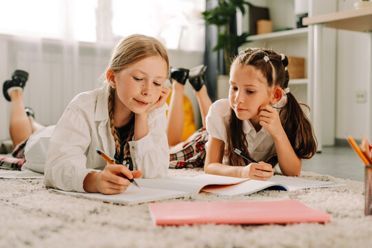 Two schoolgirls lying on carpet doing homework