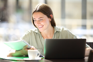 Happy student in a bar reading notes using laptop