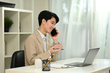 Smiling male financial counselor talking on a mobile phone and using laptop in office