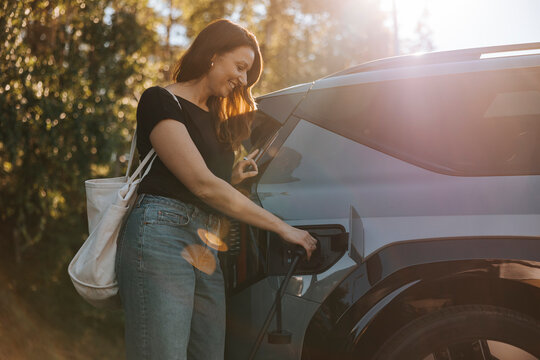 Smiling mature woman charging car while standing at station