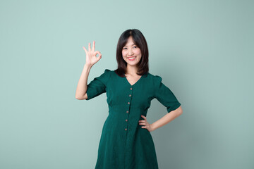 woman in green dress is smiling and making OK gesture with her hand, exuding confidence and...