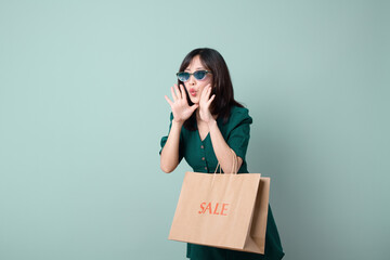 Excited woman in sunglasses holding shopping bag, celebrating sale. Her joyful expression captures thrill of shopping and finding great deals