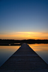Naklejka premium Wooden jetty at sunset on a Swedish lake. Sunset reflected in the water