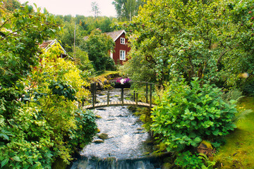 Stream with a small bridge in front of a red wooden house in Sweden. Trees