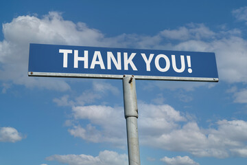 A blue metal sign mounted on a weathered metal post displaying the phrase THANK YOU! in bold white letters. against a clear blue sky with scattered clouds