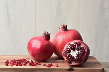 Photograph of the red pomegranates on a wooden board, the whole and open with juicy edible seeds. Sweet, tart fruit, high in antioxidants such as polyphenols. Healthy eating. Five a day. 