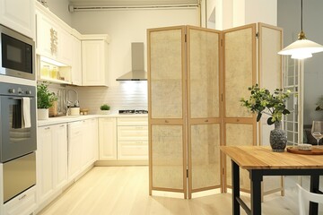 Modern kitchen interior with folding screen. Wooden plank panel divides space. Comfortable chair and table near counter. Stylish decor and vase on rack.