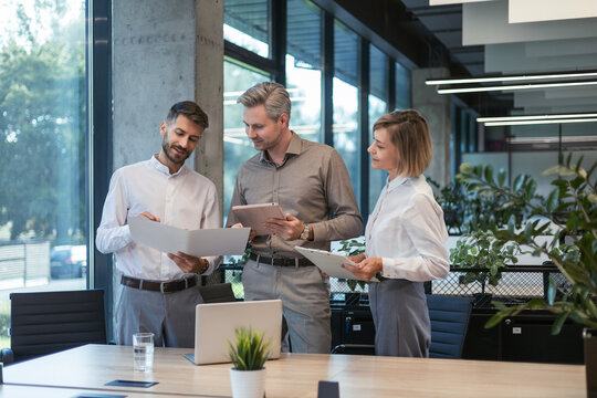 Three business people discussing work together using a tablet and laptop taking notes in a modern office