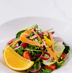 Fresh vegan salad with orange and pine nuts on white background