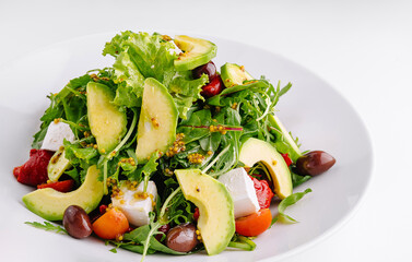 Fresh salad with avocado, feta cheese and olives served on white plate