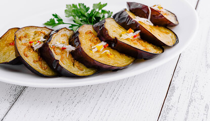 Slices of grilled eggplant with garlic and herbs on white plate