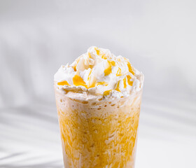 Glass of iced coffee beverage with whipped cream and caramel topping standing on white cube