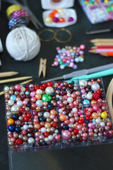 Colorful beads, coloring pencils, glitter, needles, string, hoop, tape and scissors on dark background. Various colorful craft supplies. Selective focus.