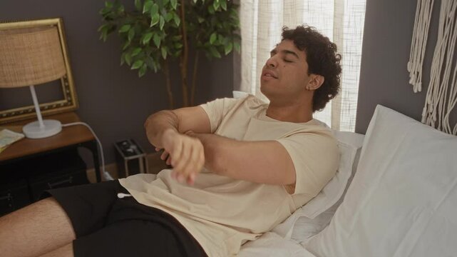 Young hispanic man sitting on bed in pyjama, looking tired and bored with depression problems, arms crossed, thinking in bedroom room