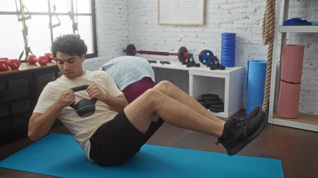 Young hispanic man exercising at gym doing sit-ups with dumbbell focus on fitness training indoors