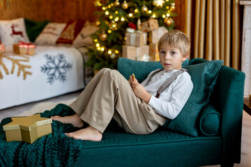 Sweet blond child, cute boy, playing with christmas toys on Christmas, beautifully decorated home for Christmas, cosy place