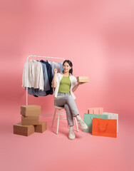 Portrait of Asian woman posing on pink background, next to shopping bags.