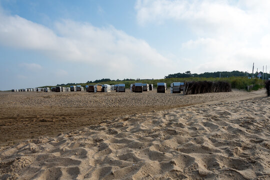 Heller, lockerer Sand im Vordergrund, dann feuchter, fester Sand, dann wieder heller Strandsand. Dahinter D&uuml;nengras und ein Wald.Der leicht bew&ouml;lkte Himmel bietet Raum f&uuml;r Texturen.