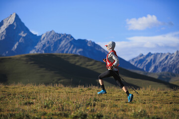Fitness woman trail runner running in grassland with snow capped mountains in the background