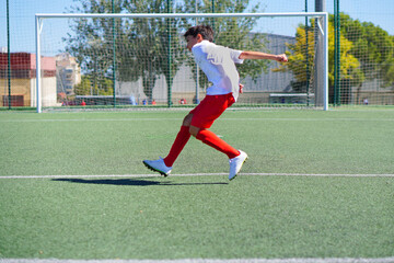 preteen boy playing a soccer game in red and white kit and soccer shoes