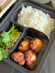 Delicious meal in a takeout container featuring rice, salad, and crispy meat. Perfect for food lovers and meal prep enthusiasts.